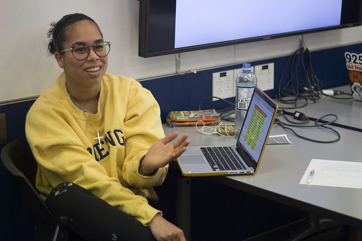 A university student at a laptop in a classroom, talking through their work.